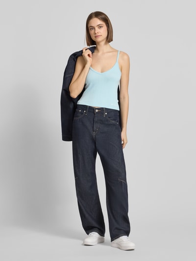 Frauenmodel trägt Trägertop mit Logo Modell 'GJ POINTELLE CAMI' von Guess Jeans in Hellblau aus Material-Mix mit Viskose-Anteil, Slim-Fit, Spaghettiträger, V-Ausschnitt, kombiniert mit dunkler Jeans, Rückenlänge bei Größe S: 26 cm, Ganzkörperansicht von vorne.