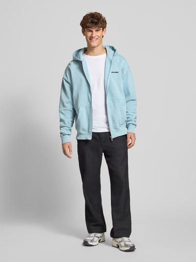 Męski model nosi Oversized Sweatjacke mit Logo od Pegador, bawełniana, oversize, logo, kaptur, zamek, kieszeń kangurka, długość tyłu 70 cm, długość rękawa 66 cm, widok całej sylwetki z przodu.