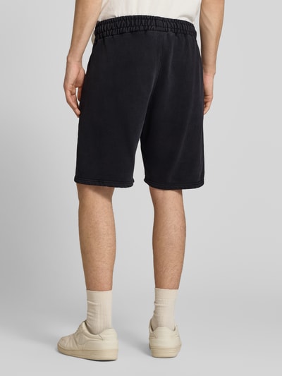 Männermodel trägt Shorts mit elastischem Bund und Logo-Stitching von Pegador aus Baumwoll-Mix in Schwarz, Loose-Fit, Ganzkörperansicht Rückansicht.