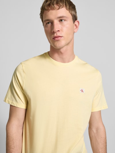 Männermodel trägt T-Shirt mit Label-Badge von Calvin Klein Jeans in Gelb, Reine Baumwolle, Regular-Fit, Rundhalsausschnitt, Nahaufnahme Oberkörper.