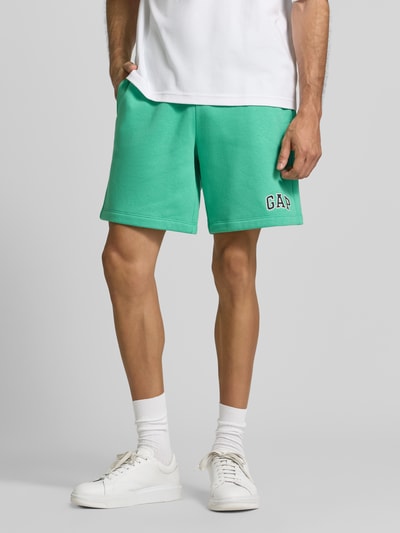 Männermodel trägt Straight Fit Shorts mit logo-Stitching Model 'Heritage' van GAP in groen katoenmix, elastische band met tunnelkoord, bandwijdte 40 cm, binnenbeenlengte 20 cm, ganzkörperansicht van voren.