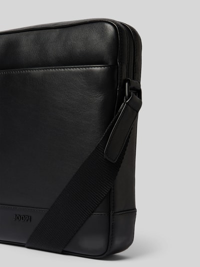 Produktfoto, Crossbody Bag mit Label-Detail Modell 'manciano' von JOOP! Collection, schwarze Farbe, glatte Textur, Reißverschluss, Verstellbarer Schulterriemen, Hauptfach und Nebenfach, Innenfach mit Reißverschluss, rechteckige Form, Maße 23x26x5 cm, Schulterriemen 130 cm.