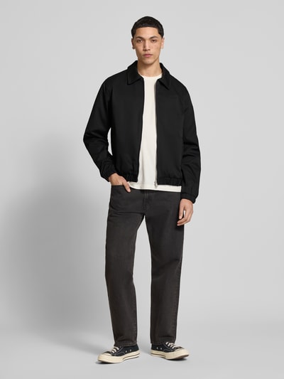 Männermodel trägt Jacke mit Zweiwege-Reißverschluss Modell 'CATSKILLS' von Jack & Jones, Regular-Fit, Umlegekragen, Label-Stitching, schwarze Farbe, Ganzkörperansicht von vorne, Rückenlänge 64 cm, Schulterbreite 49 cm, Brustweite 59 cm, Ärmellänge 66 cm.