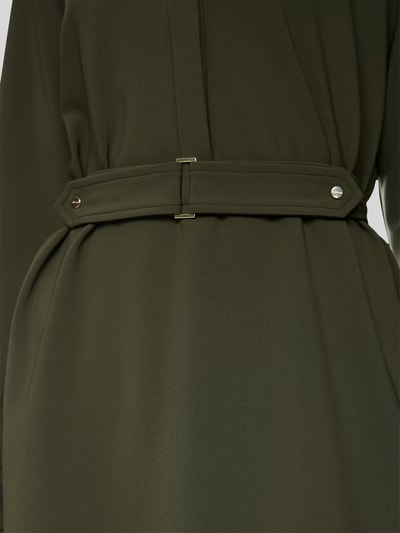 Frauenmodel trägt Knielanges Kleid mit Stehkragen und Gürtel von Marc Cain, olivgrüner Material-Mix mit Stretch, Detailaufnahme Oberkörper.