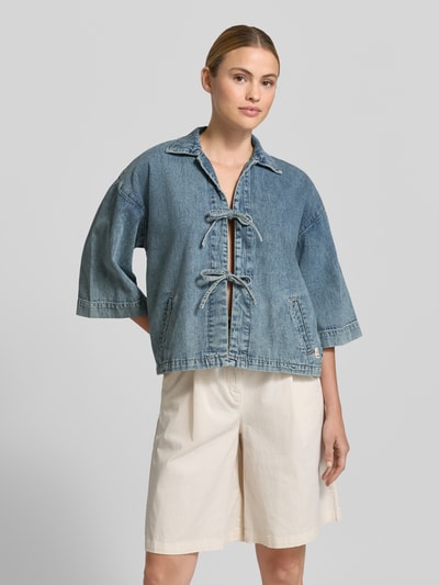 Frauenmodel trägt Jeansjacke mit Kimonoärmel Modell 'ZOE' von Mustang aus Reine Baumwolle, Regular-Fit, Umlegekragen, Schnürverschluss, Seitliche Eingrifftaschen; Rückenlänge 56 cm, Schulterbreite 44 cm, Brustweite 54 cm, Ärmellänge 43 cm; Ganzkörperansicht von vorne.