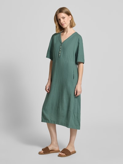Frauenmodel trägt knielanges Kleid aus Leinen-Viskose-Mix Modell 'Lava' von FREE/QUENT in A-Linie mit V-Ausschnitt, Knopfleiste, grün, glatte Textur, Ganzkörperansicht von vorne, Rückenlänge 96 cm, Brustweite 43 cm, Ärmellänge 29 cm.