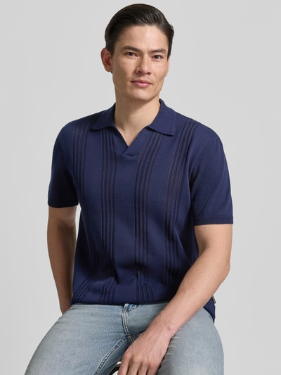 Männermodel trägt Relaxed Fit Poloshirt aus reiner Baumwolle von Armedangels, unifarbenes Feinstrick, kurzer Ärmel, Ganzkörperansicht von vorne.