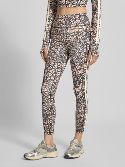 Frauenmodel trägt Slim Fit Sport-Leggings mit floralem Muster Modell 'FARM LEGGINGS' von adidas Sportswear, dunkle Töne und bunte Blumen, Nahaufnahme Unterkörper, KI-modifiziertes Bild.