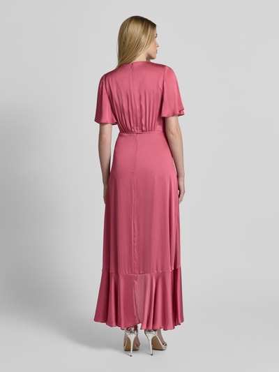 Frauenmodel trägt Abendkleid in Wickel-Optik mit Bindegürtel von Christian Berg Cocktail in Satin, taillierter Schnitt, Maxikleid in Rosa, Volantsaum, Rückansicht, Ganzkörperansicht Rückansicht.