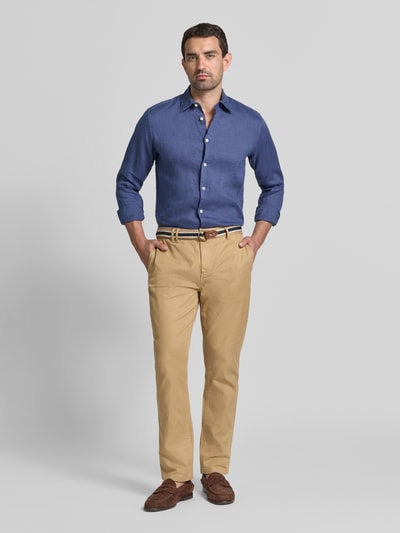 Männermodel trägt Chino mit Gürtel und Eingrifftaschen Modell 'WARREN' von Scotch & Soda in Beige, Straight Fit, Ganzkörperansicht von vorne. Baumwoll-Mix mit Stretch-Anteil, Knopf- und Reißverschluss, Doppel-D-Schnalle, seitliche Eingrifftaschen, Gesäßtaschen.