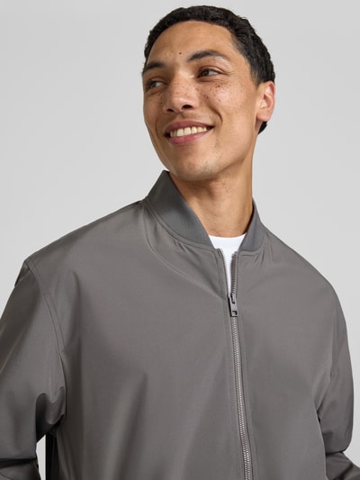 Männermodel trägt graue Bomberjacke mit Stehkragen Modell 'CHARGE' von Jack & Jones, Regular-Fit, Nahaufnahme Oberkörper. Rückenlänge 67 cm, Schulterbreite 53 cm, Brustweite 62 cm, Ärmellänge 65 cm, Reißverschluss.