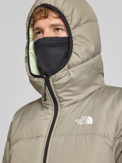Männermodel trägt Regular Fit Jacke in Stepp-Optik von The North Face in Beige mit Kapuze und Logo-Print, Nahaufnahme Oberkörper. Herren Jacke, Stepp-Optik, Kapuze mit Stehkragen, Reißverschluss, Rückenlänge 68 cm, Schulterbreite 46 cm, Brustweite 55 cm, Ärmellänge 70 cm.
