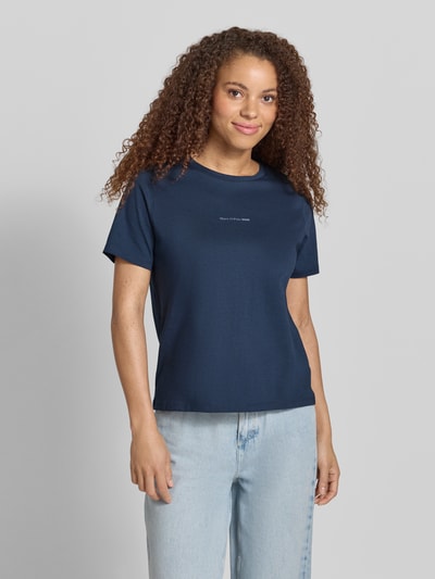 Kobiece model nosi Regular Fit T-Shirt aus reiner Baumwolle od Marc O'Polo Denim, jednokolorowy, krój regular fit, z napisem z logo, okrągły dekolt, krótki rękaw, dżersej z czystej bawełny, granatowy, gładka struktura, widok całej sylwetki z przodu.