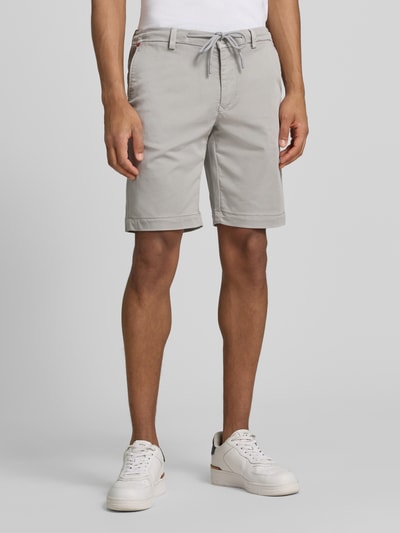 Männermodel trägt Bermudas mit Bindegürtel und französischen Eingrifftaschen von MAC, Baumwoll-Mix mit Stretch-Anteil, Straight Fit, Knopf- und Reißverschluss, Bundweite 42 cm, Innenbeinlänge 26 cm, Label-Print, helle Farbe, glatte Textur, Ganzkörperansicht von vorne.