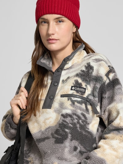 Kobiece modelka nosi Regular Fit Pullover mit Logo-Patch Modell 'Helvetia' od Columbia w stylu fleece, beżowo-czarno-szary wzór, kieszeń na piersi z suwakiem, elastyczne mankiety, stójka, guziki, Szerokość w rozmiarze S: 58 cm, długość pleców: 55 cm, Szerokość ramion: 44 cm, długość rękawa: 58 cm; zbliżenie na górną część ciała