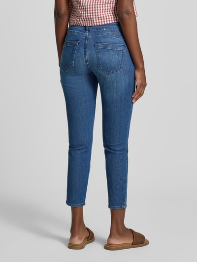 Frauenmodel trägt Slim Fit Jeans aus Baumwoll-Mix Modell 'SHAKIRA' von Brax in Denim-Optik mit Label-Patch und Gürtelschlaufen, Ganzkörperansicht Rückansicht.