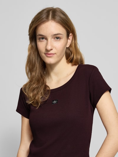 Modelka nosi Cropped T-Shirt mit Label-Detail von Calvin Klein Jeans, bawełna z elastanem, okrągły dekolt, bordowy, zbliżenie górnej części ciała.