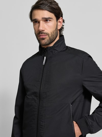 Männermodel trägt Regular Fit Jacke mit Stehkragen von MCNEAL in Schwarz mit Reißverschluss und Eingrifftaschen, Nahaufnahme Oberkörper. Rückenlänge 64 cm, Schulterbreite 43 cm, Brustweite 55 cm, Ärmellänge 67 cm.