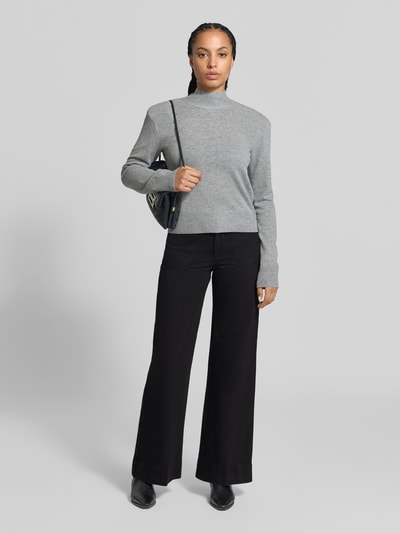 Frauenmodel trägt Wide Fit Jeans aus reiner Escorial Wolle von Victoria Beckham in Schwarz, aufgesetzte und Gesäßtaschen, Knopf- und Reißverschluss, kombiniert mit grauem Pullover, Innenbeinlänge 82 cm, Bundweite 35 cm, Ganzkörperansicht von vorne.