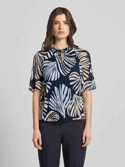 Modelka nosi Regular Fit Blusenshirt in Plissee-Optik od s.Oliver BLACK LABEL, efekt: wzór na całej powierzchni, krój regular fit, kołnierz z falbanami, plisy, okrągły dekolt z wycięciem w kształcie łezki, wiązanie, krótki rękaw, tekstura plisowana, widok całej sylwetki z przodu.