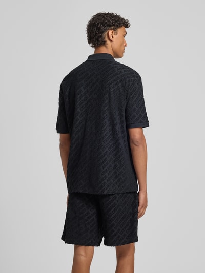 Männermodel trägt Slim Fit Poloshirt mit Logo-Muster von ARMANI EXCHANGE, Baumwoll-Mix, schwarz, strukturierte Textur, Ganzkörperansicht Rückansicht.