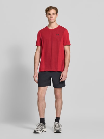 Männermodel trägt Regular Fit Sport-T-Shirt mit Logo-Print von Under Armour in Rot zu dunklen Shorts, Ganzkörperansicht von vorne. Herren Sport-T-Shirt von Under Armour