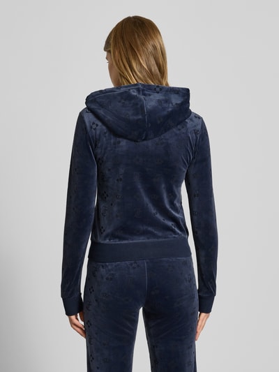 Kobiece model nosi bluzę rozpinaną z kapturem model 'MONO MADISON' od Juicy Couture, granatowa, mieszanka materiałów z dodatkiem streczu, krój slim fit, kieszeń kangurka, widok całej sylwetki od tyłu.
