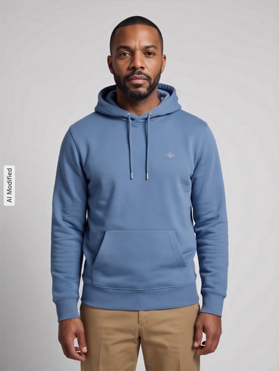 Männermodel trägt Regular Fit Hoodie aus Baumwoll-Mix von GANT in Hellblau, Kängurutasche, Ganzkörperansicht von vorne, KI-modifiziertes Bild.