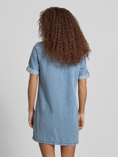 Frauenmodel trägt Jeanskleid mit Brusttaschen Modell 'NEW SIGNE' von Noisy May aus Reine Baumwolle, Gerader-Schnitt, Minikleid, Rückenlänge bei Größe S 86 cm, Brustweite 50 cm, Ärmellänge 25 cm, blauer Denim mit sichtbarer Webstruktur, Ganzkörperansicht Rückansicht.