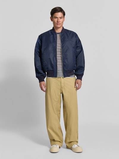 Männermodel trägt Straight Fit Hose aus reiner Baumwolle von Diesel in Beige, kombiniert mit dunkler Jacke, Ganzkörperansicht von vorne. Reine Baumwolle, Gürtelschlaufen, Gesäßtaschen, Knopf- und Reißverschluss, Innenbeinlänge 78 cm, Bundweite 44 cm.