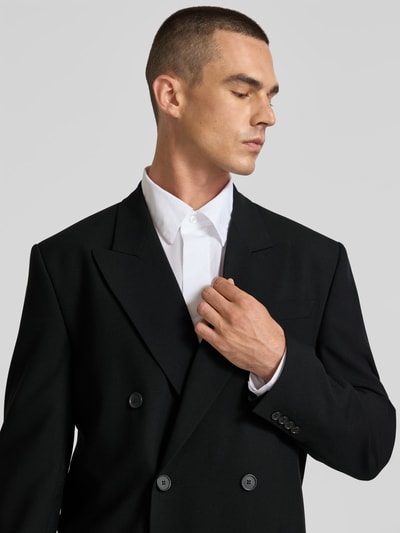 Męski model nosi Straight Fit Sakko aus Woll-Mix od Filippa K, kolor czarny, dwurzędowa listwa guzikowa, kołnierz z połami, nakładane kieszenie, długość tyłu w rozmiarze 50: 80 cm, szerokość ramion w rozmiarze 50: 43 cm, długość rękawów w rozmiarze 50: 66 cm, materiał o gładkiej teksturze, zbliżenie na górną część ciała, widok z przodu.