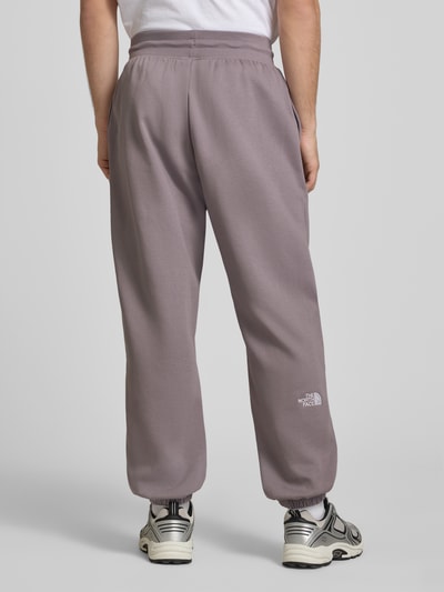 Männermodel trägt Sweatpants mit Logo-Stitching von The North Face in Flieder, Baumwoll-Mix, Relaxed-Fit, elastischer Bund, elastische Abschlüsse, Ganzkörperansicht Rückansicht.