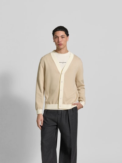 Männermodel trägt Cardigan aus reiner Baumwolle von MAISON KITSUNÉ in Beige mit V-Ausschnitt und Knopfleiste, lockere Passform, Ganzkörperansicht von vorne