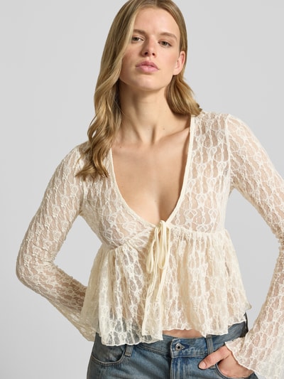 Frauenmodel trägt Shaped Fit Blusentop mit Bindeverschluss Modell 'LAYA' von Only in semitransparenter Mesh-Optik, abstraktes Muster, tiefer V-Ausschnitt, langarm, cremefarben, Nahaufnahme Oberkörper.