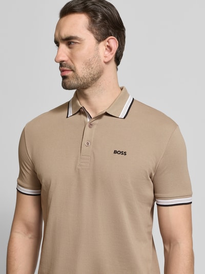 Męski model nosi Regular Fit Poloshirt aus reiner Baumwolle Modell 'PADDY' von BOSS, beżowa gładka bawełna piké, krój regular fit, kołnierzyk polo, krótki rękaw, nadruk z logo, zapięcie na 3 guziki, półzbliżenie przód