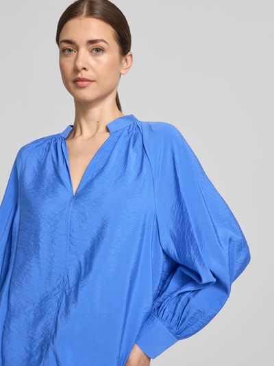 Frauenmodel trägt Bluse aus Viskose-Mix mit Serafino-Ausschnitt von Christian Berg Woman in Blau, lockere Passform, Sportmanschetten, Nahaufnahme Oberkörper.