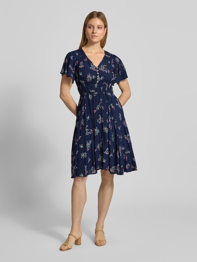Frauenmodel trägt Knielanges Kleid aus Viskose mit V-Ausschnitt von Apricot in A-Linie, Allover-Look, elastisches Taillenband, Ganzkörperansicht von vorne. Rückenlänge Größe S: 104 cm, Brustweite: 44 cm, Ärmellänge: 21 cm.