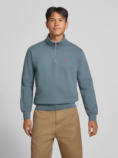 Männermodel trägt Regular Fit Pullover aus reiner Baumwolle von Levi's® in Blau, kombiniert mit beigefarbener Hose, Ganzkörperansicht von vorne.