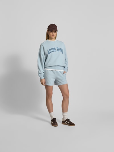 Frauenmodel trägt Oversized Sweatshirt mit Logo-Detail von Anine Bing, reine Baumwolle, Oversized-Fit, Rundhalsausschnitt, elastische Abschlüsse; hellblaue Farbe, Rückenlänge bei Größe S: 65 cm, glatte Textur, Ganzkörperansicht von vorne.