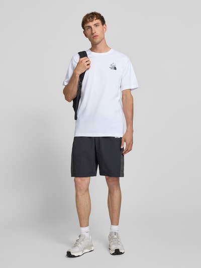 Mannenmodel draagt T-shirt met Label-Print en Rundhalsausschnitt van The North Face in wit, puur katoen, regular fit, ruglengte maat M 71 cm. Ganzkörperansicht von vorne.