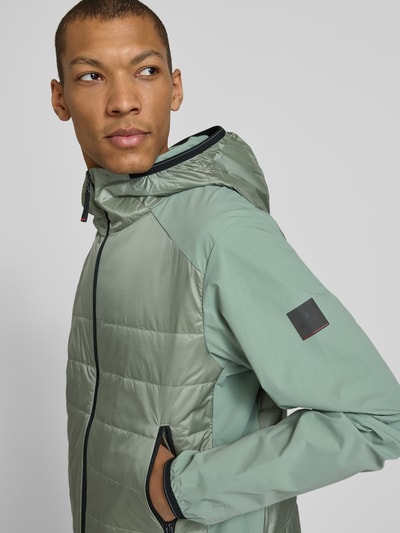 Männermodel trägt Jacke mit Zweiwege-Reißverschluss Modell 'KEGAN2' von FIRE + ICE in Grün, Steppnähte, Kapuze, Nahaufnahme Oberkörper.