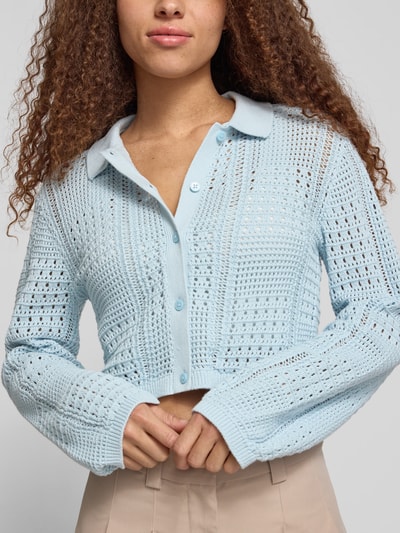 Vrouwenmodel draagt Regular Fit Cardigan met Polokraag model 'Sue' van JJXX van puur katoen, lichtblauw, met gaatjesmotief, met lange mouwen, knoopsluiting, elastische mouwboord, ruglengte maat S 43 cm, mouwlengte maat S 63 cm, voorkant bovenlichaam close-up.