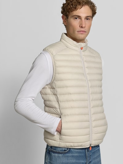 Männermodel trägt hellbeige Steppweste mit Zweiwege-Reißverschluss Modell 'ADAM' von Save The Duck, Regular Fit, Stehkragen, Ganzkörperansicht von vorne