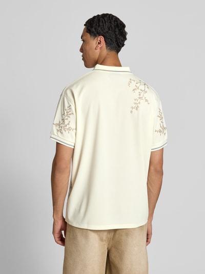 Männermodel trägt Poloshirt floralem Allover-Stitching von Don’t Waste Culture in Beige mit Relaxed-Fit, Logo-Print, Kurzärmelig, Rückenlänge 71 cm, Ganzkörperansicht Rückansicht.