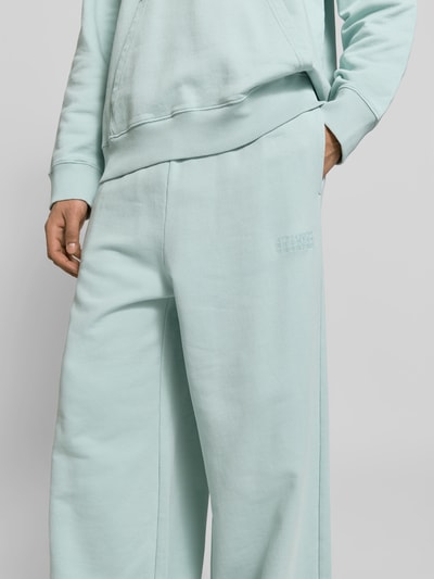 Männermodel trägt Wide Fit Sweatpants mit elastischem Bund von MM6 Maison Margiela aus reiner Baumwolle mit Logo-Stitching und Gesäßtasche, Nahaufnahme Oberkörper.