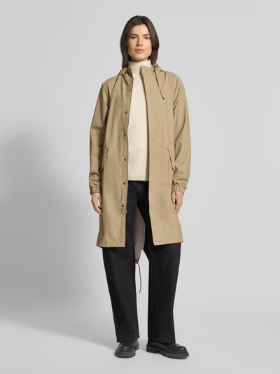 Frauenmodel trägt Regular Fit Parker mit Kapuze Modell 'Fishtail' von Rains in Beige mit Pattentaschen und elastischen Ärmelabschlüssen, Ganzkörperansicht von vorne. Rückenlänge 104 cm, Schulterbreite 45 cm, Brustweite 55 cm, Ärmellänge 65 cm, glatte Textur.