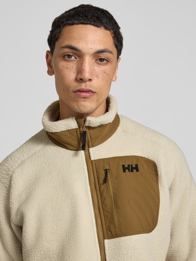 Männermodel trägt Fleecejacke mit Stehkragen von Helly Hansen in Beige und Braun, lockere Passform, Nahaufnahme Oberkörper.