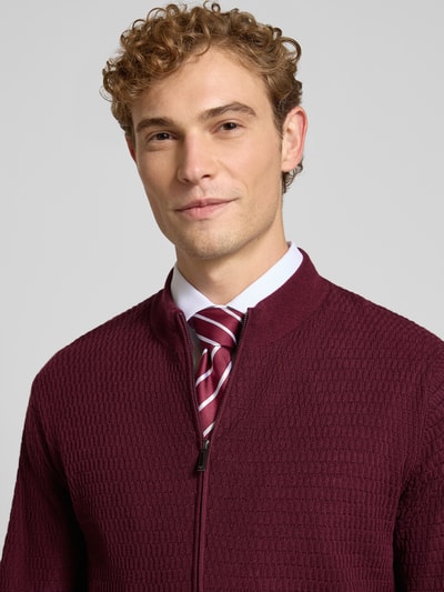 Männermodel trägt Regular Fit Strickjacke aus reiner Schurwolle von Emporio Armani in Bordeaux mit Strukturmuster, Nahaufnahme Oberkörper. Schmale Passform, Zwei-Wege-Reißverschluss, gerippte Abschlüsse, Rückenlänge 64 cm, Ärmellänge 67 cm.