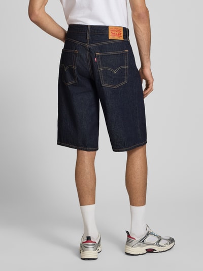 Männermodel trägt Baggy Jeansshorts aus reiner Baumwolle Modell '470' von Levi's®, dunkle Denim-Optik, Label-Patch, 5-Pocket-Design, Ganzkörperansicht Rückansicht.