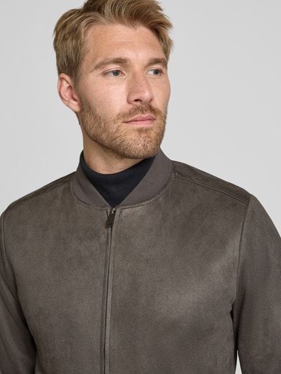 Męskimodel nosi Regular Fit Bomberjacke mit Stehkragen von Christian Berg Men z elastycznej mieszanki materiałów, zamek błyskawiczny, wpuszczane kieszenie, stójka, długość tyłu w rozmiarze M 60 cm, długość rękawów w rozmiarze M 67 cm, matowa faktura, odcienie brązu, gładka powierzchnia, Nahaufnahme górnej części ciała.